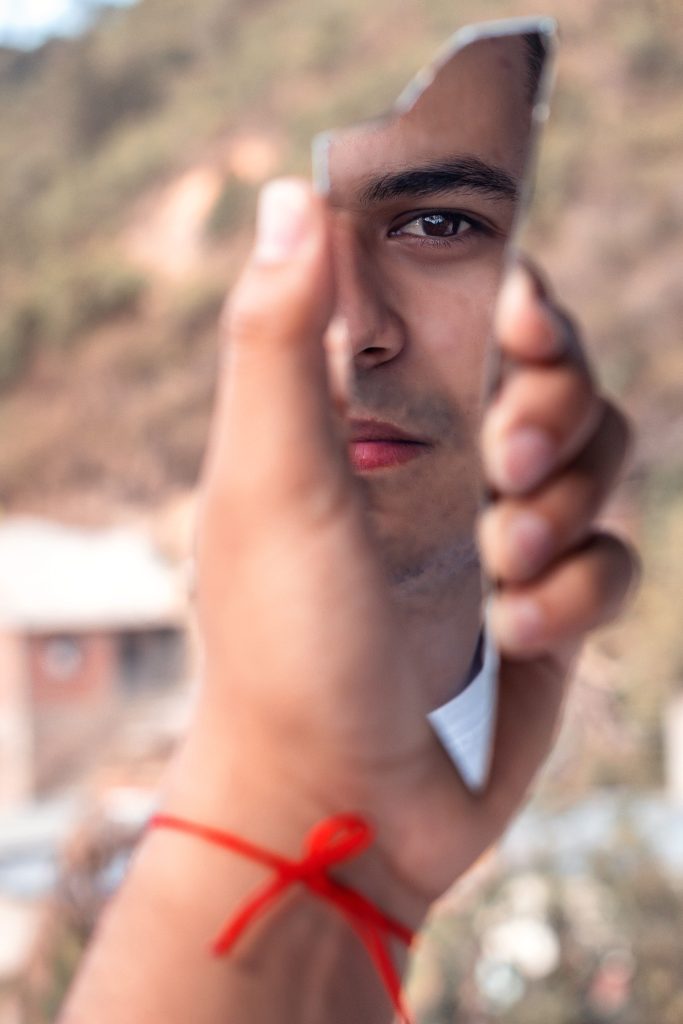 Man's face reflecting in a broken mirror shard, capturing identity theme.